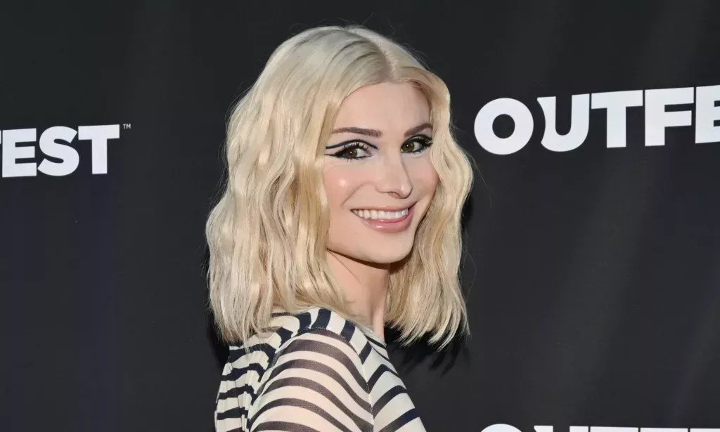 Dylan Mulvaney with a choppy blonde bob and black and white top smiling at the camera.