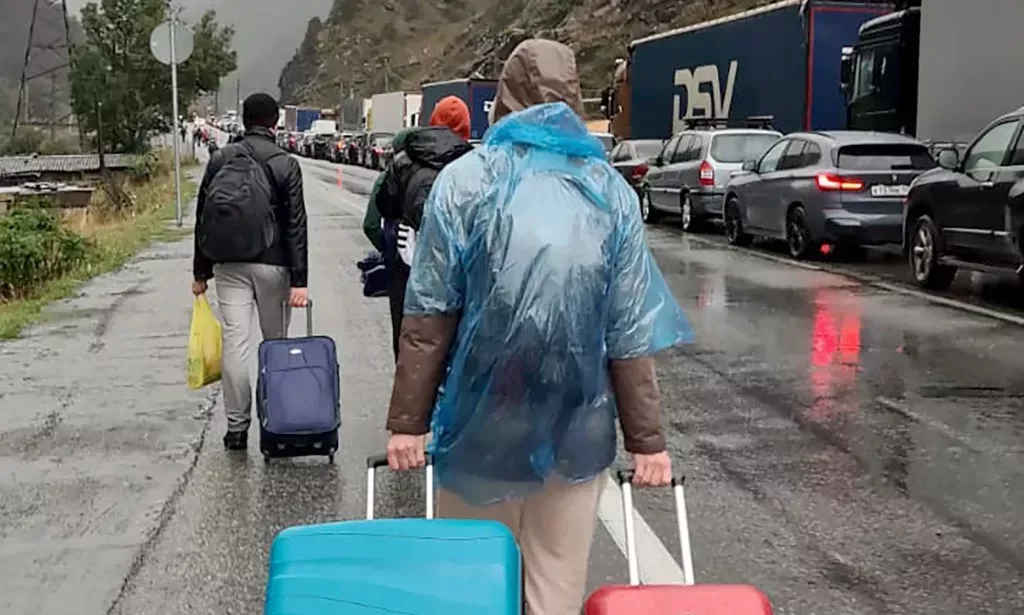 Several people wheel rolling bags along the side of a roadway as they try to leave Russia via a land border crossing