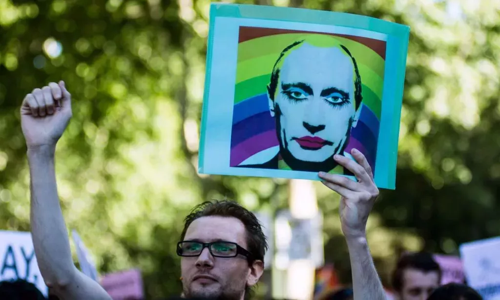 A person holds up a sign with a stylised picture of Russia's president Vladimir Putin with makeup on and a rainbow LGBTQ+ background