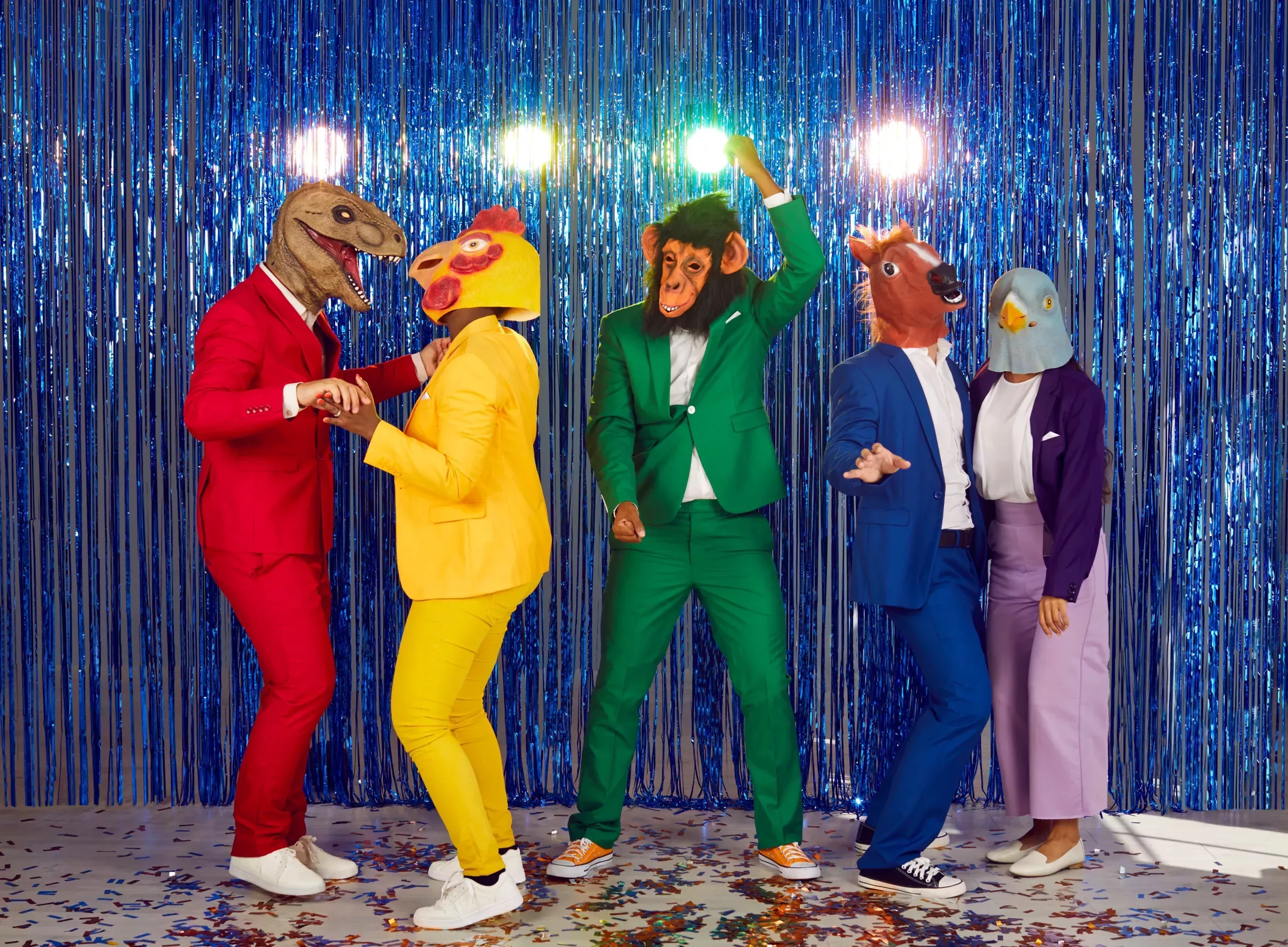 A group of people dancing wearing different animal heads and suit colors from the rainbow.