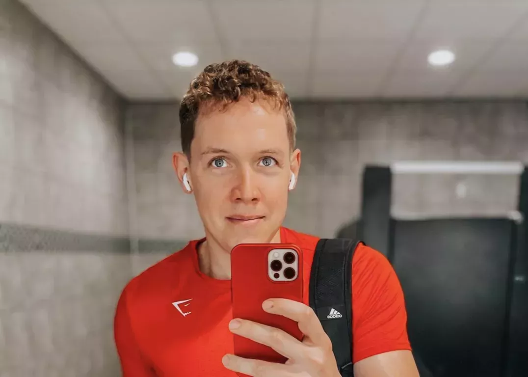 Basketball coach Matt Lynch wearing a red athletic shirt and AirPods while taking a bathroom selfie. 