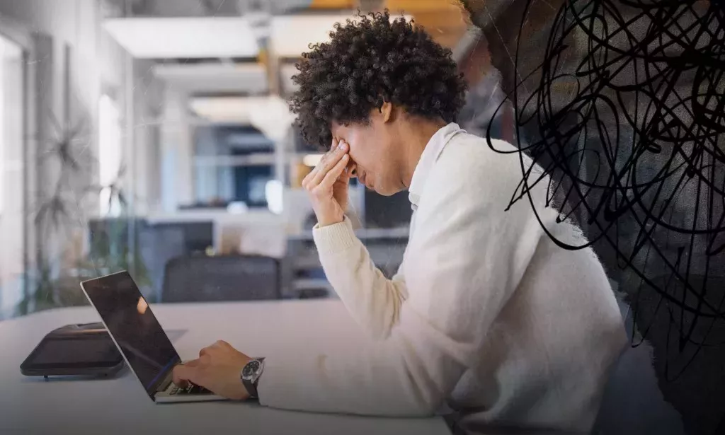 A man in an office with a laptop looking stressed