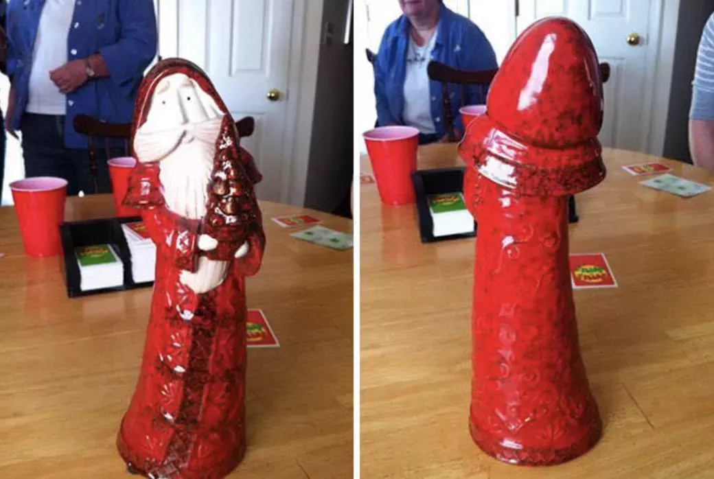 Two-panel image. In the left panel, a tall and skinny glass Santa decoration wearing a red hooded suit and carrying a staff with a Christmas tree on it sways to one side. The figure is pictured on a wooden table with a card game askew. In the second panel, the same figure is turned around to reveal the back of its hooded red suit, resembling a long hooded phallus.