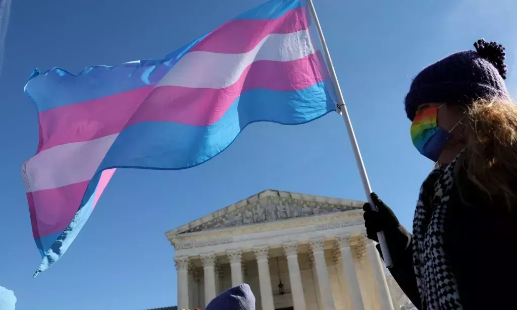 Una persona afuera de la Corte Suprema ondeando una bandera trans.
