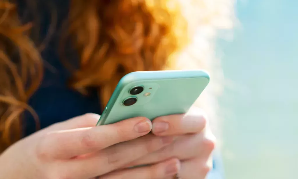 mujer sosteniendo un teléfono: La actualización de iOS 17.4 de Apple incluye 118 nuevos emojis