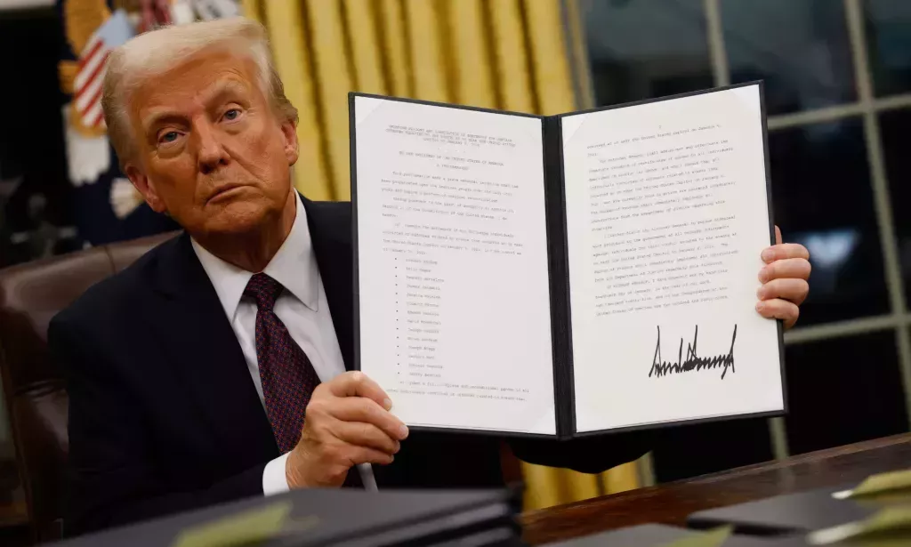 Donald Trump sosteniendo un documento que contiene un decreto ejecutivo.