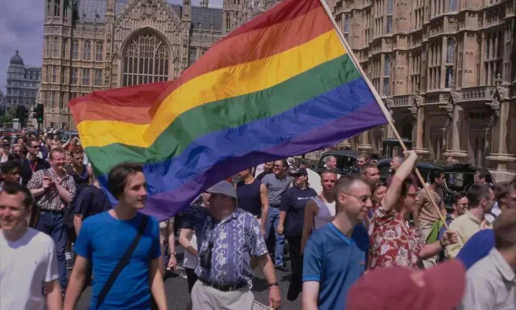 Una multitud de protestores LGBTQ+, uno de los cuales agita una bandera del Orgullo.