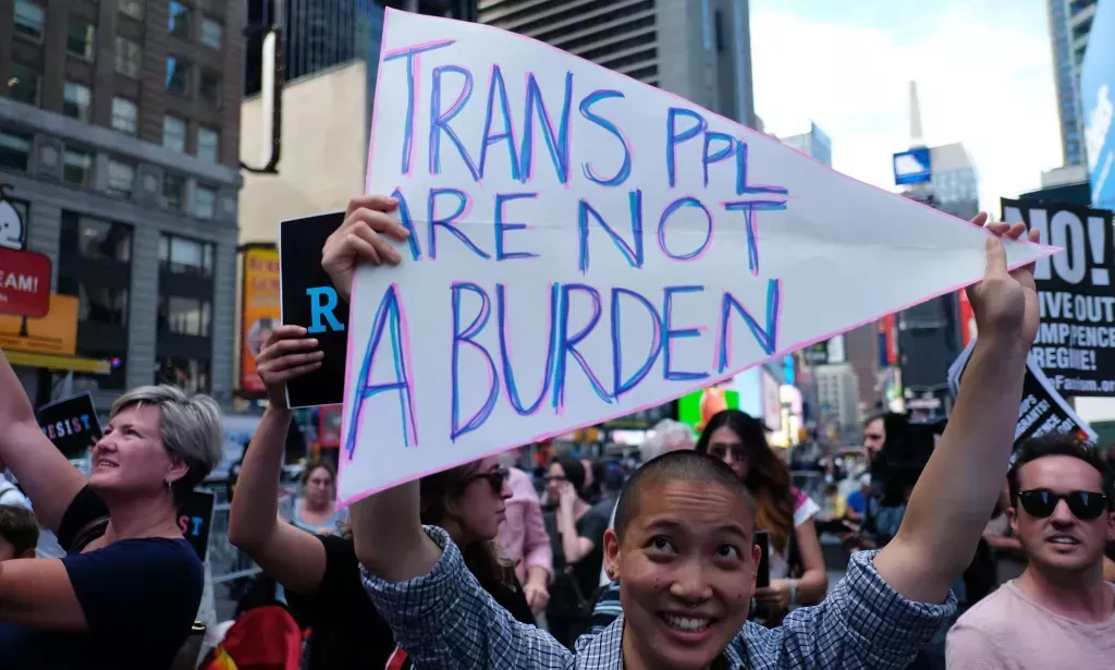 Una persona sosteniendo un cartel que dice 'las personas trans no son una carga.'