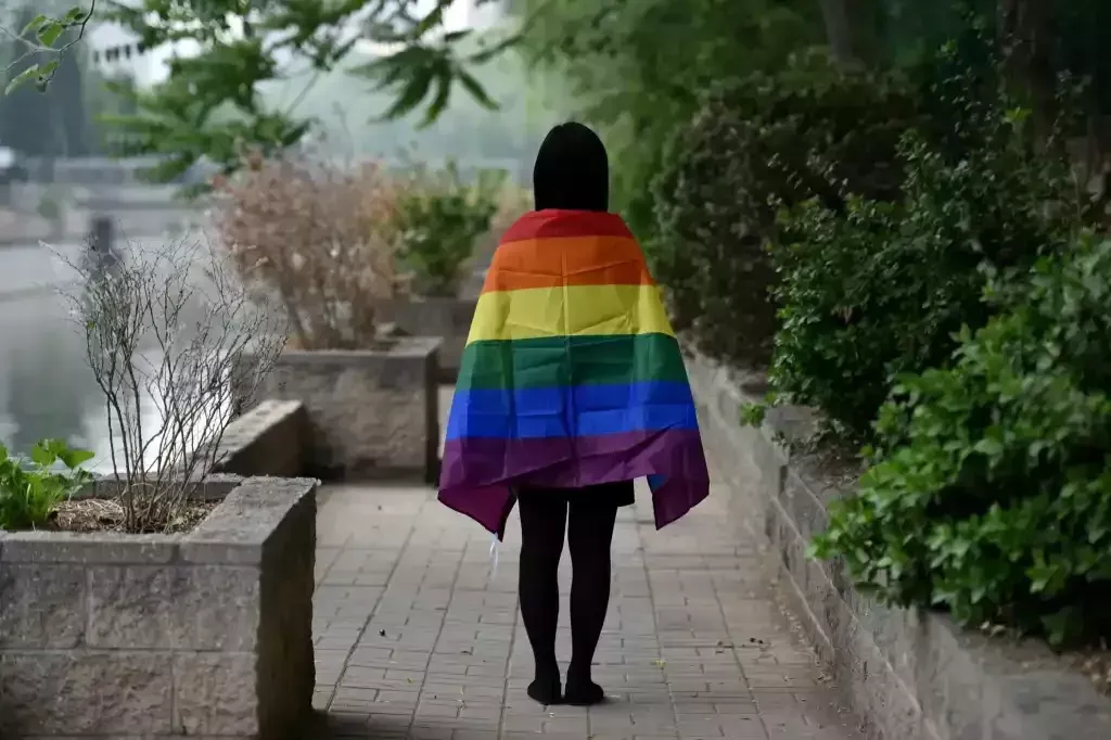 Estudiante con una bandera LGBT+ sobre sus hombros, fotografiado por detrás, en Beijing, China