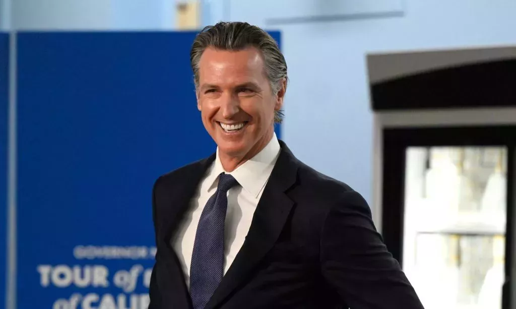 Gobernador de California Gavin Newsom, que apoyó un proyecto de ley anti-prohibición de libros, sonríe mientras usa una camisa blanca, corbata azul y chaqueta oscura